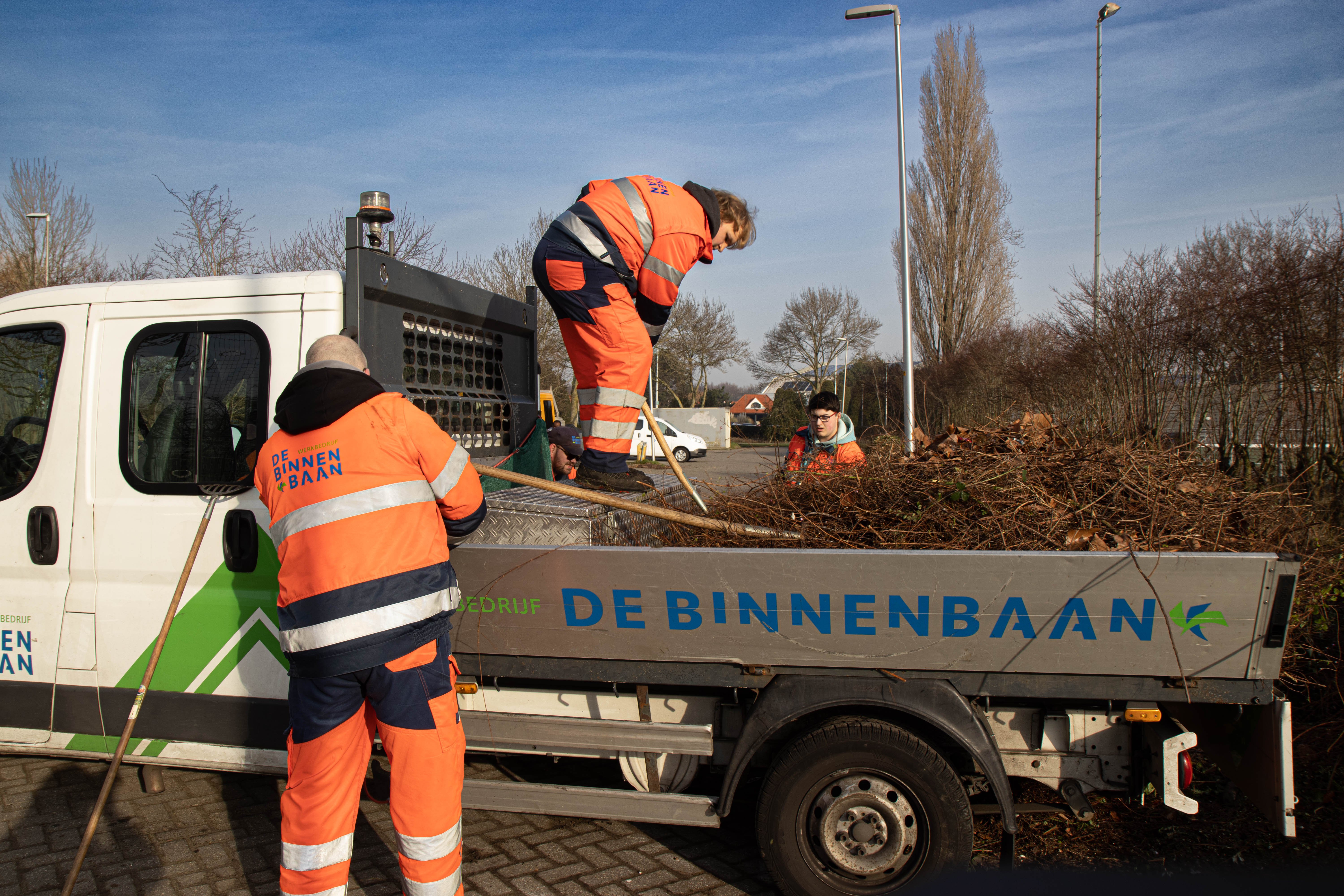 Medewerkers van de Groenacademie van De Binnenbaan voeren groenonderhoud uit en laden snoeiafval in een bedrijfswagen.